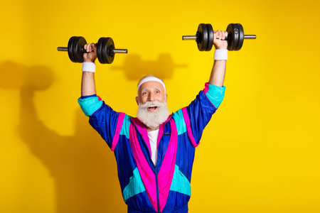 Photo portrait banner of funny senior sportsman lifting dumbbells dressed stylish retro sport costume isolated on yellow color backgroundの写真素材