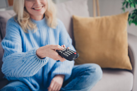 Cropped photo of aged woman hand hold tv remote control wear pullover free time modern apartment indoorsの写真素材