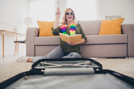 Photo of crazy excited woman sitting on floor writing plans for weekend tour organizing valise indoors flat apartmentの写真素材