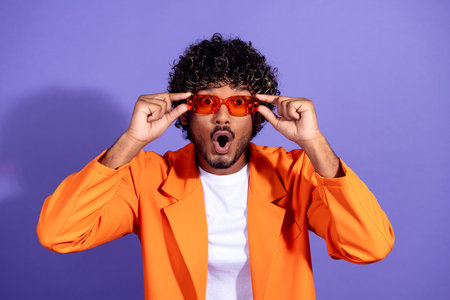 Photo of impressed funny guy wear orange suit arms dark eyewear emtpy space isolated violet color backgroundの写真素材