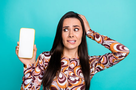 Photo of dountful pretty lady dressed retro shirt biting lip looking modern gadget empty space isolated blue color backgroundの写真素材
