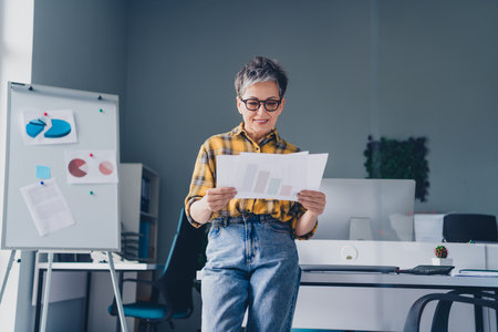 Photo of pretty senior female hold papers trading wear plaid yellow shirt coworking successful nice...