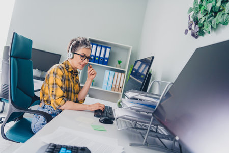 Photo of lovely pensioner lady it specialist work computer headset wear plaid yellow shirt coworking successful nice light officeの写真素材