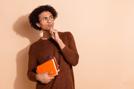 Young african american man deep in thought holding colorful notebooks against a beige backgroundの写真素材