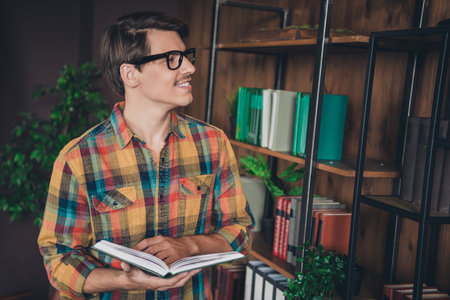 Photo of handsome young smart man nerd wear checkered shirt choose book indoors college university libraryの写真素材
