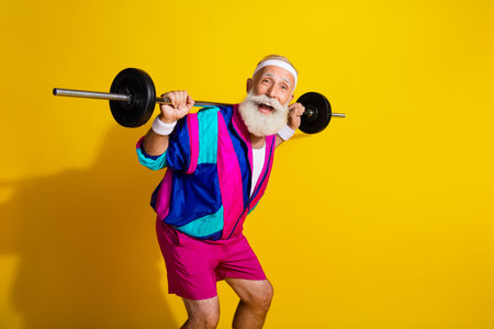 Photo poster of handsome granddad sportsman hold shoulders barbell wear trendy vintage sportswear isolated on yellow color backgroundの写真素材