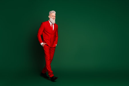 Full body profile portrait of classy trendy santa walk empty space wear red new year xmas suit isolated on green color backgroundの写真素材