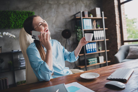 Photo of positive good mood lady specialist dressed shirt laughing enjoying beverage listening modern device indoors workstation workshopの写真素材