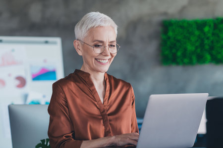 Photo of mature old female hold netbook project management dressed brown shirt office professional workshop room interiorの写真素材