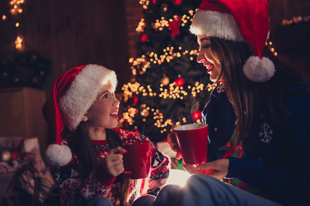 Photo of lovely family mother daughter drinking cacao dressed christmas outfit day light home party decoration interior roomの写真素材