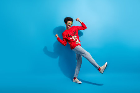 Full body photo of attractive young man dance excited dressed red christmas sweater theme party on blue color backgroundの写真素材