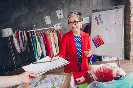 Photo of aged clothing designer lady give concept paper client hand loft interior office studio indoorsの写真素材