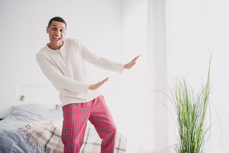 Photo of nice young man dancing have fun wear pajama enjoy wake up modern cozy interior bedroom indoorsの写真素材