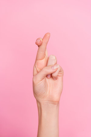 Vertical cropped view of attractive girl hand showing crossed fingers r letter isolated over pink pastel color backgroundの写真素材