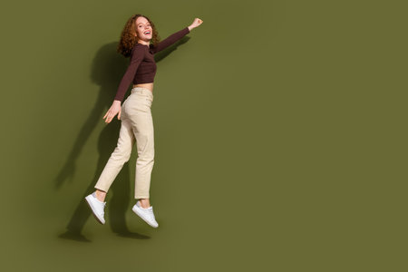 Full length photo of adorable excited girl wear brown shirt rising fist empty space isolated khaki color backgroundの写真素材