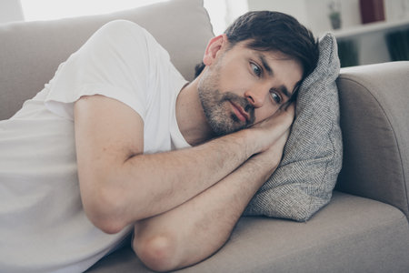 Relaxed man lounging on sofa at home, enjoying a calm weekend afternoon with a peaceful and contemplative expressionの写真素材
