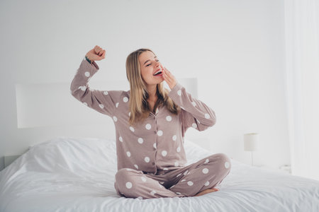 Young woman in polka dot pajamas waking up joyfully in her cozy bedroomの写真素材