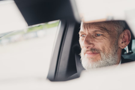 Mature businessman in formal suit contemplating the road ahead while seated in a car, reflecting on business travel opportunities and personal goalsの写真素材
