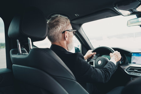 Mature businessman driving in city, focused on travel. Professional in suit behind wheel of luxury car, embodying success.の写真素材