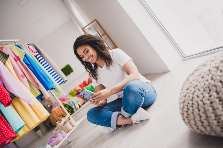 Young african american woman smiling at home while browsing clothes on sale in daylight living room.の写真素材