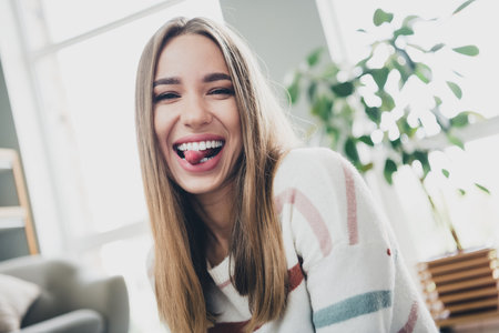 Cheerful young woman in natural light enjoying a relaxing day at home, smiling playfully in the cozy...