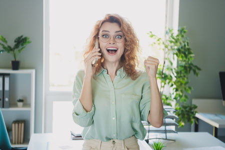 Portrait of corporate worker young woman communicate phone raise fist wear shirt business center...