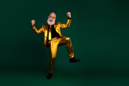 Charismatic senior in shining golden suit celebrates with excitement against a vibrant green backdrop, retro glamour and festive spirit.の写真素材