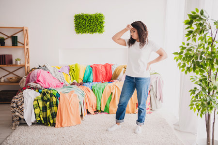 Young woman in living room surrounded by colorful clothes considers options for donation, sale, or keeping during daylightの写真素材