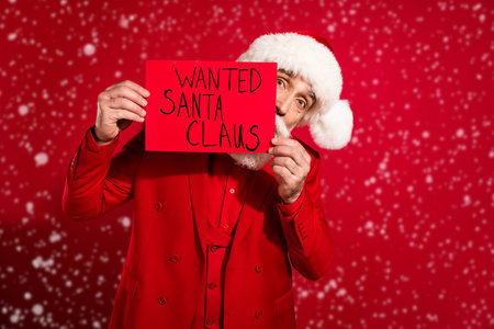 Photo of serious shy age gentleman wear new year costume headwear hiding wanted santa claus card isolated red color backgroundの写真素材