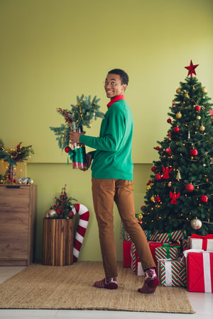 Photo of positive young man wearing green clothes preparing for xmas holidays decorating room indoorsの写真素材