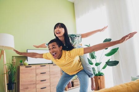 Photo of good mood cheerful multinational couple wife and husband enjoy weekend together piggyback indoors flatの写真素材