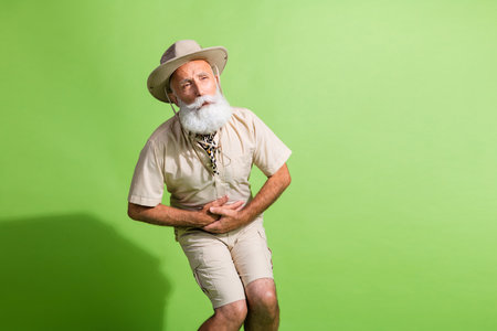 Photo of old traveler touch belly feel hurt digestion vomit wear safari suit isolated green color backgroundの写真素材