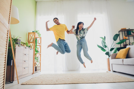 Photo of crazy funny positive multinational couple have fun jump up good mood weekend vacation indoors apartmentの写真素材