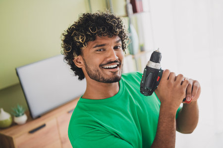Photo of nice young man hold screwdriver drill wear t-shirt modern green interior apartment indoorsの写真素材