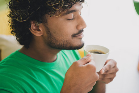 Close up cropped photo of nice young man smell coffee wear t-shirt weekend green interior apartment indoorsの写真素材