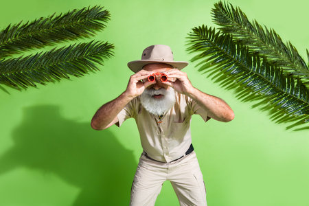 Photo of adventurer senior man watch binoculars glasses observe wildlife tropics isolated green color backgroundの写真素材