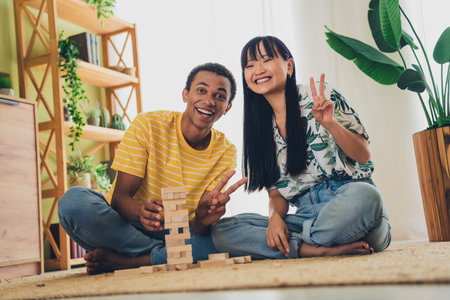 Photo of lovely cute positive multinational family sit floor play jenga build pile stack v-sign indoors flatの写真素材