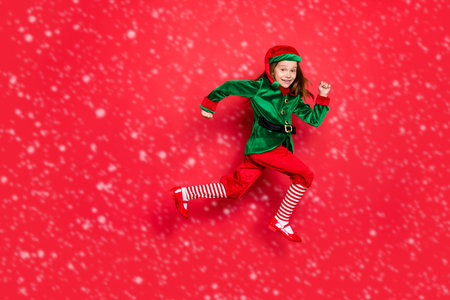 Full length body size view of nice attractive cheerful cheery funny funky carefree small little pre-teen elf having fun running marathon isolated over bright vivid shine red backgroundの写真素材