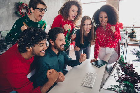 Photo of six corporate workers computer screen raise fists celebrate xmas atmosphere office party indoorsの写真素材