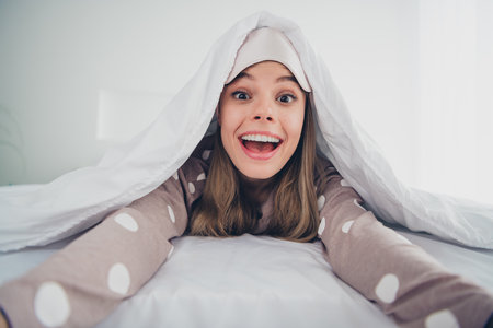 Young woman enjoying a bright morning in cozy bed at home, smiling under a blanketの写真素材