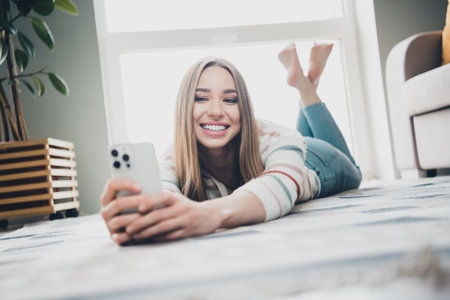 Young woman relaxing at home in daylight, enjoying a weekend on her phone in the living roomの写真素材