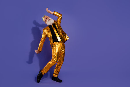 Full body photo of bearded gentleman dancing have fun wear fashionable golden clothes isolated on violet color backgroundの写真素材