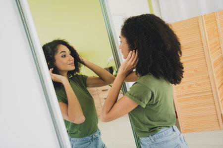 Portrait of nice young woman touch hair look mirror wear t-shirt free time modern interior flat indoorsの写真素材