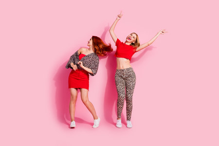 Photo of carefree lovely girls wear leopard red trendy clothes dance party empty space isolated on pink color backgroundの写真素材