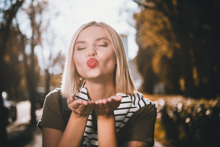 Photo of attractive young cheerful lady send you air kiss wear khaki garment tied shoulders sweater having fun outside outdoorsの写真素材