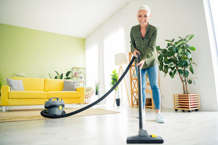 Photo of pretty cheerful lady wear green shirt enjoying vaccuum cleaning indoors room home houseの写真素材