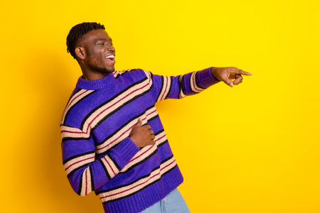 Portrait of nice young man laugh direct finger empty space wear sweater isolated on yellow color backgroundの写真素材
