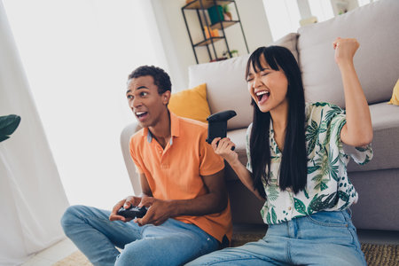 Photo of crazy cheerful couple wear t-shirts enjoy weekend together play playstation indoors living room apartmentの写真素材