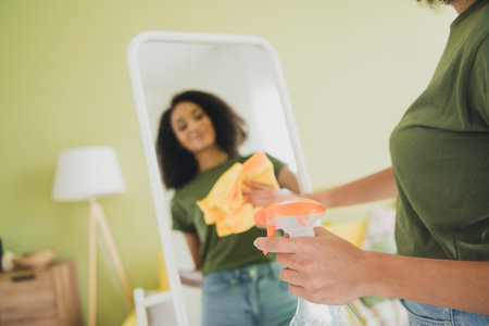 Photo of nice young girl cleaning mirror reflection wear green clothes modern daylight cozy interior...
