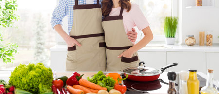 Portrait of positive friendship vegan couple spouses enjoy family hobby cooking day hug embrace ready prepare organic nutrition meal in house kitchen indoorsの写真素材